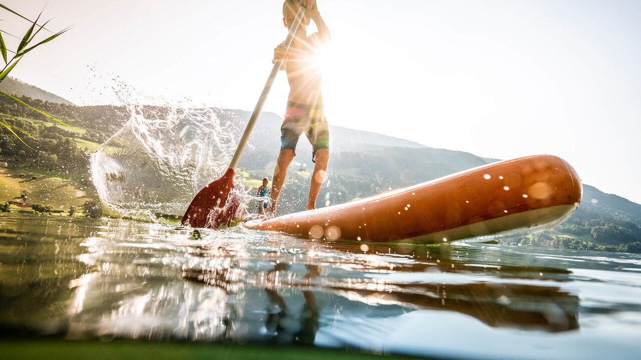 Stand-up paddleboarder on a lake against the light
