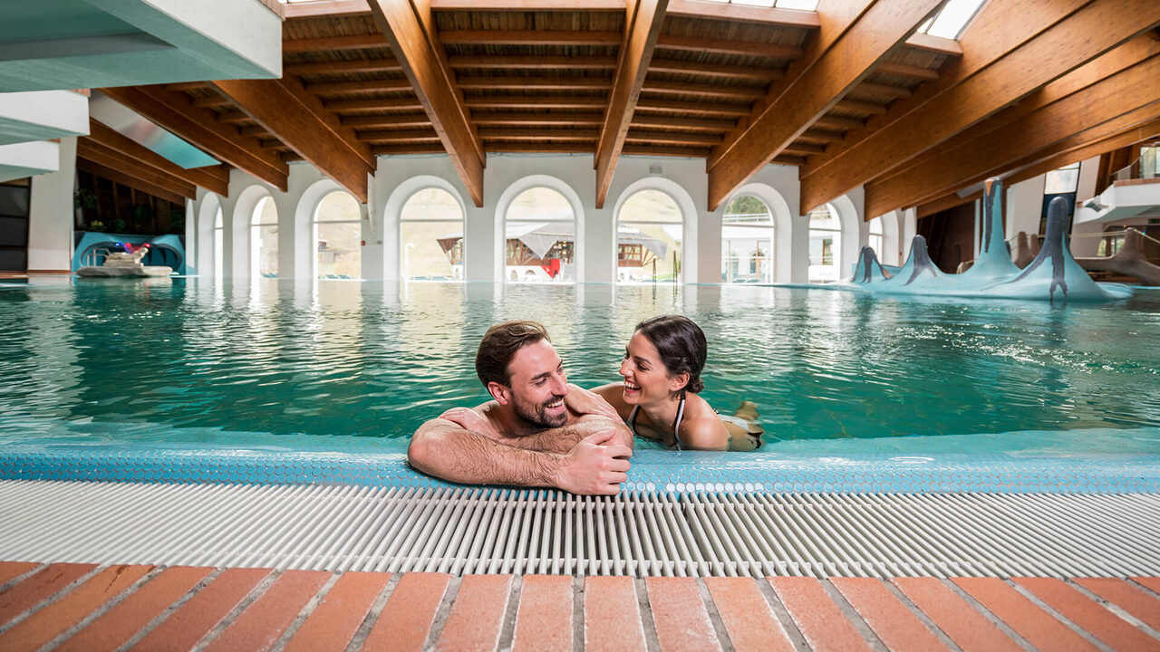 Couple at the edge of an indoor thermal pool under a wooden ceiling