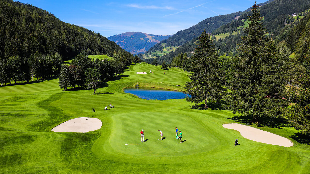 Golf course with players on the green, surrounded by forest and mountains