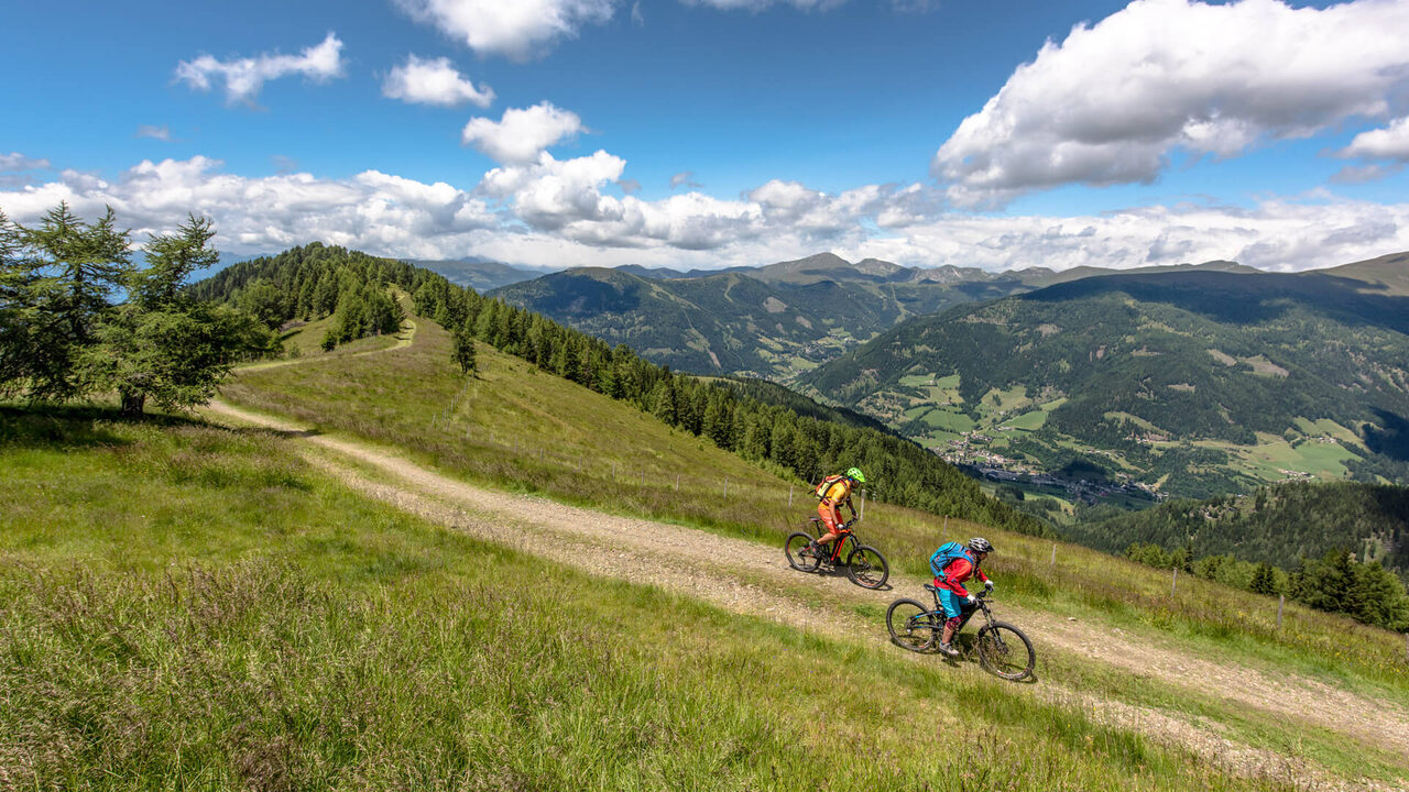 Zwei Mountainbiker auf einem Wiesentrail mit Blick über die Berge