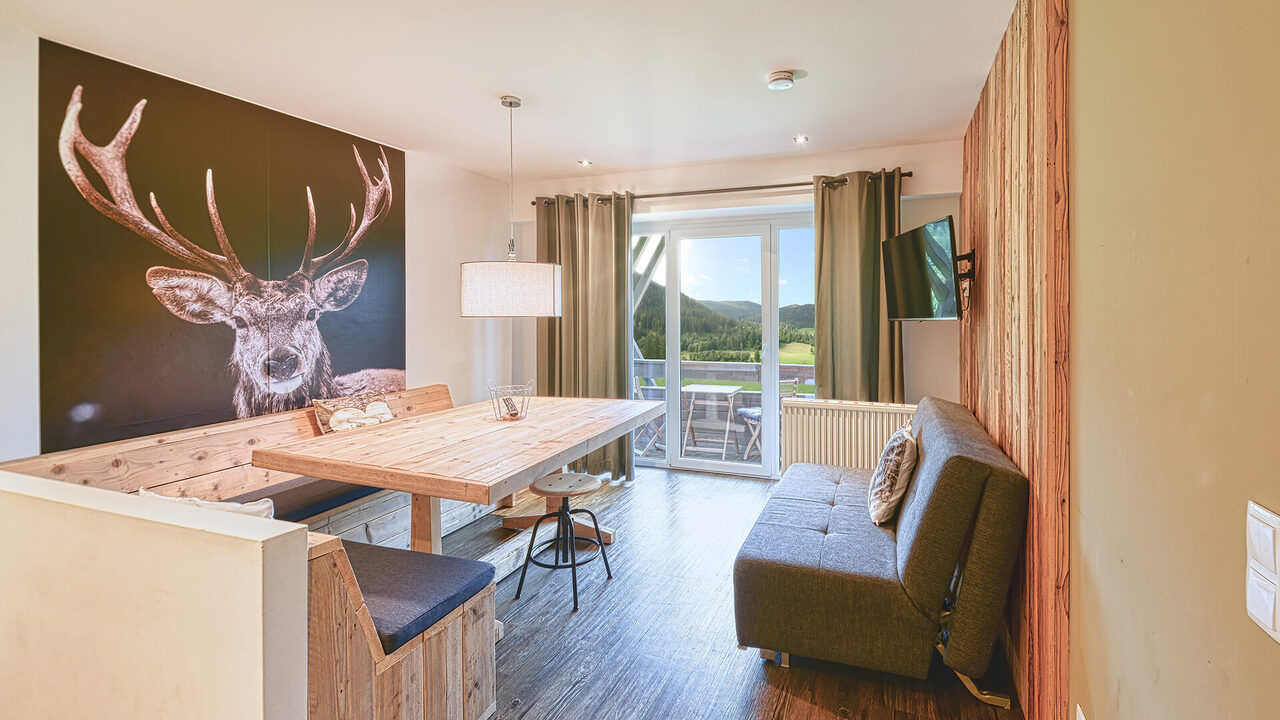 Essecke mit Hirsch-Wandbild, Schlafsofa und Terrassentür im Apartment Panorama