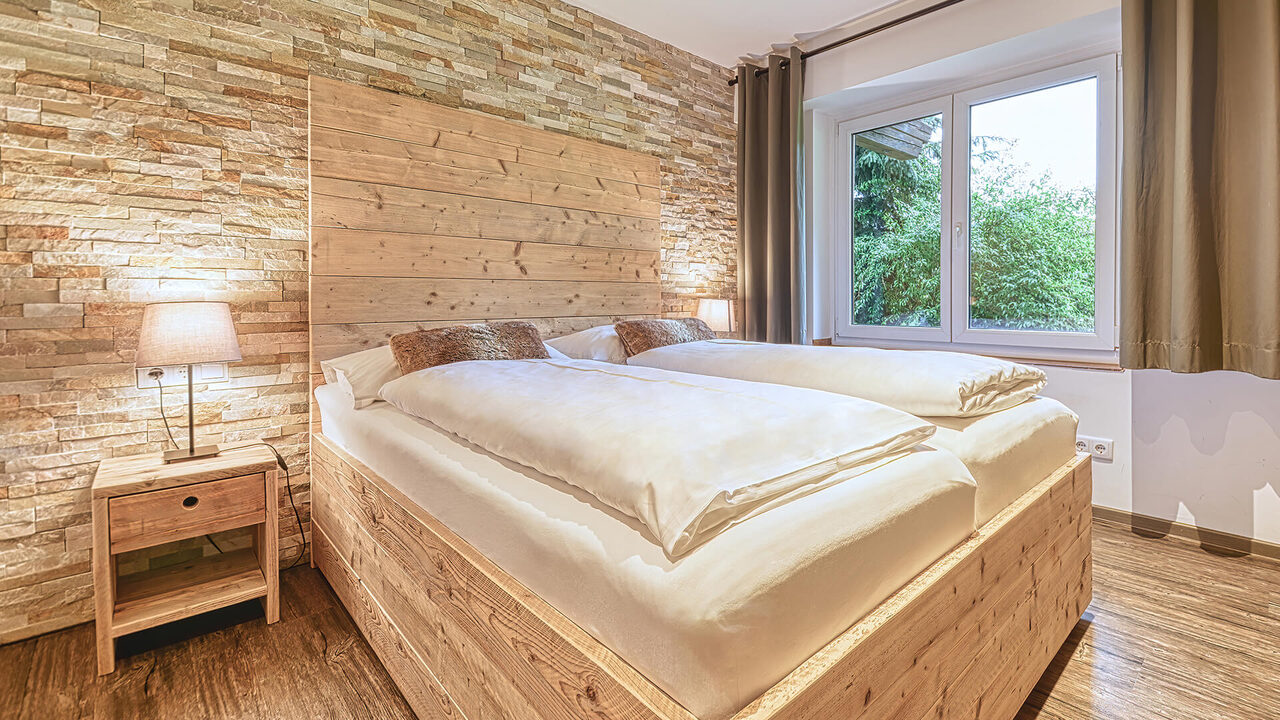 Schlafzimmer mit Doppelbett und Holzwand im Apartment Sonnwiesen