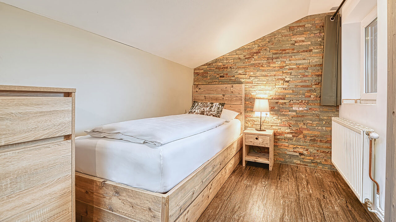 Schlafzimmer mit Einzelbett und Natursteinwand im Apartment Wiesernock