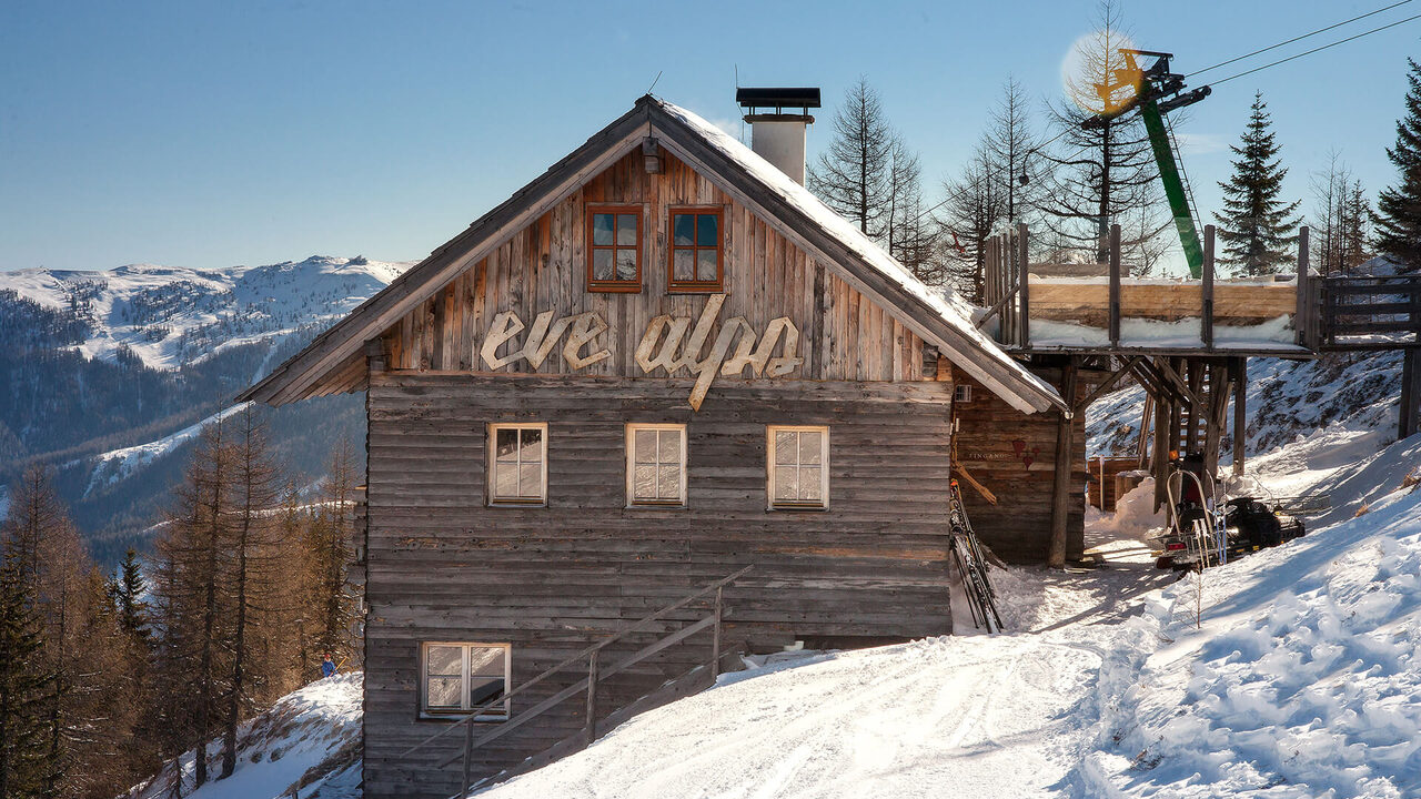 Baita di legno innevata accanto a uno skilift