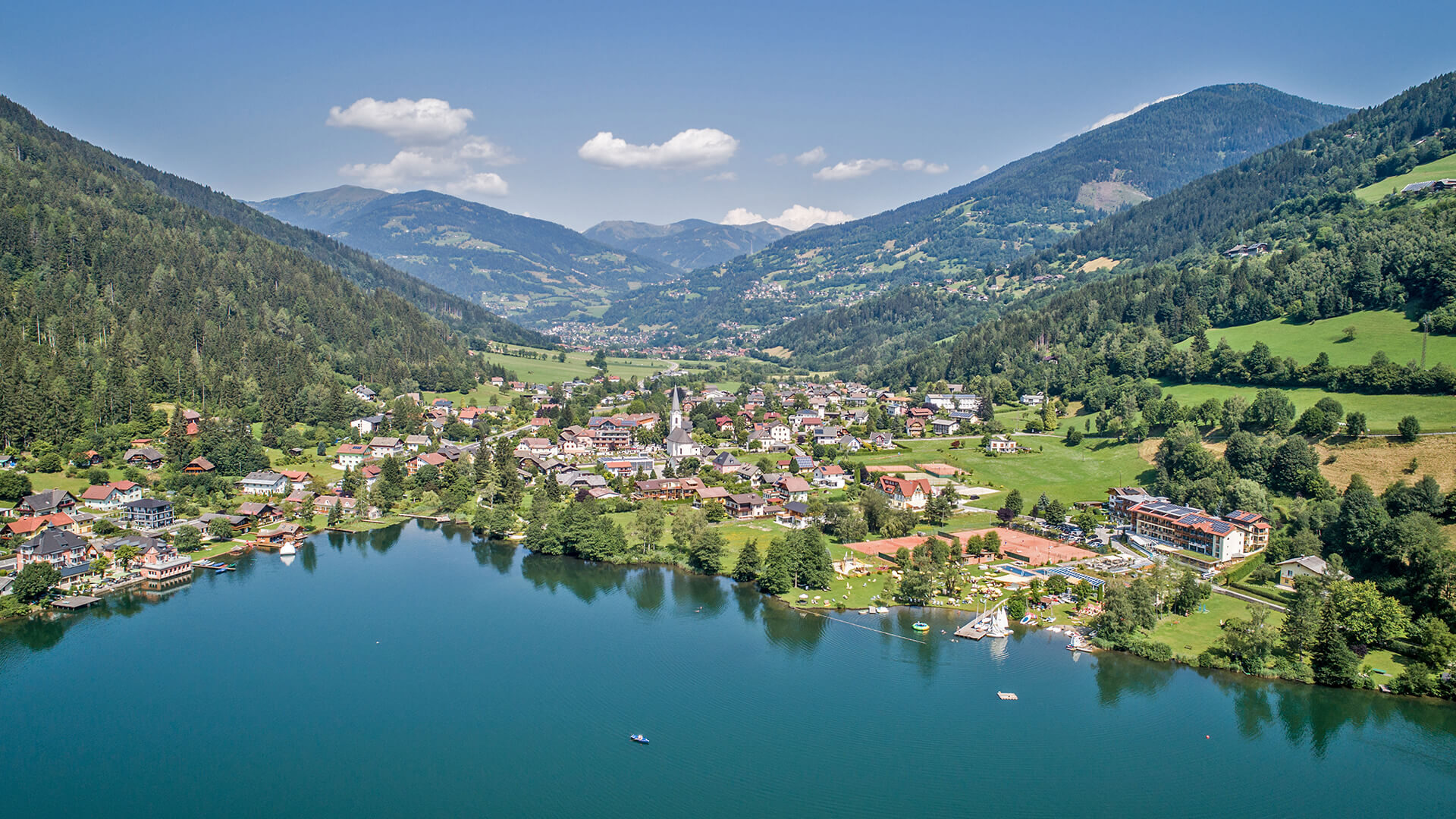 Veduta aerea di un paese sul lago circondato da montagne boscose