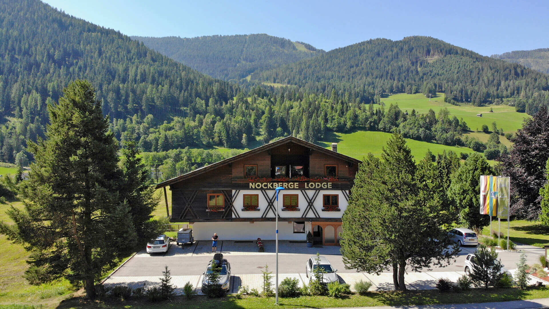 La Nockberge Lodge con il parcheggio, sullo sfondo di montagne boscose