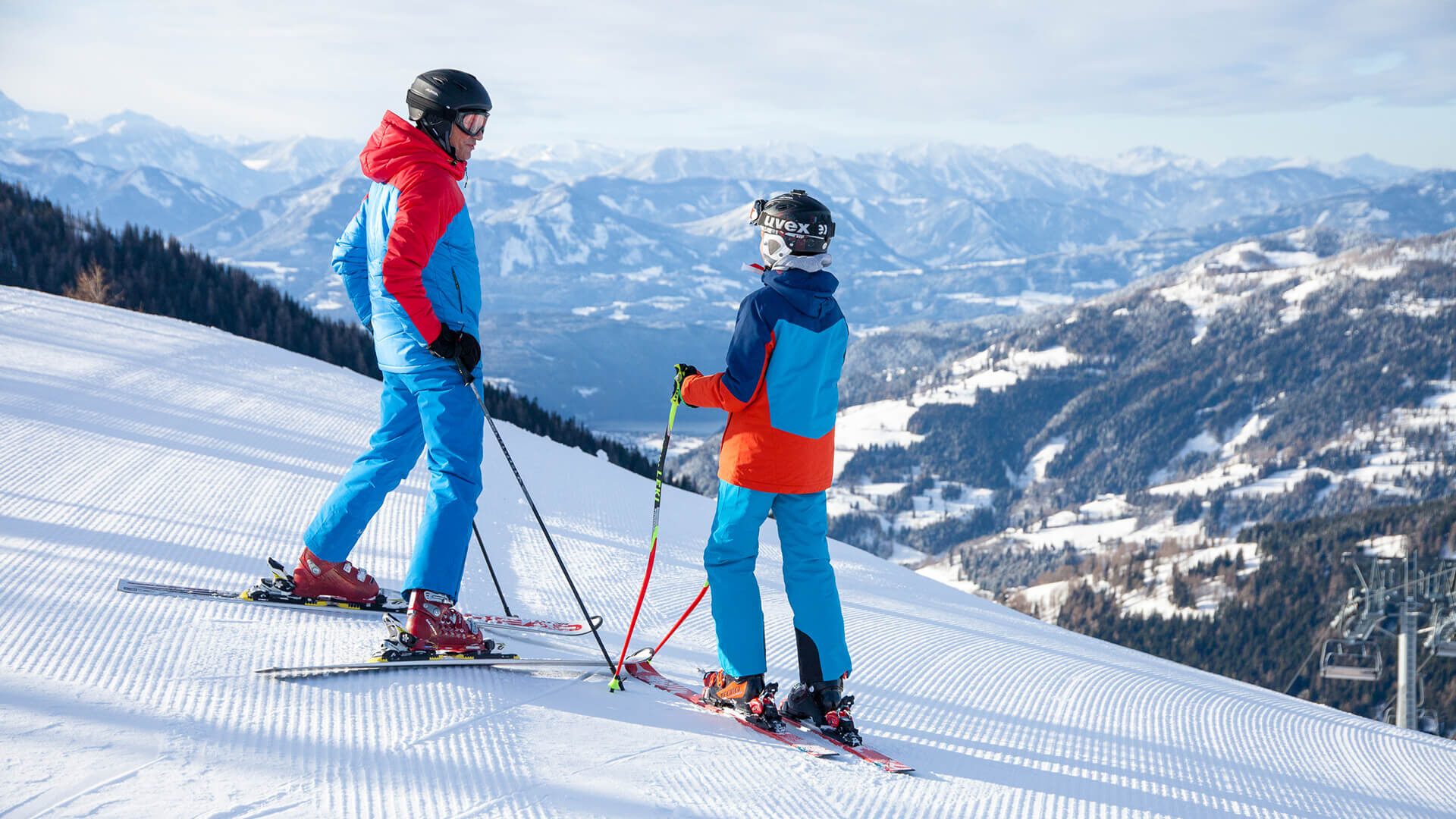 Two skiers on a groomed slope with a mountain panorama