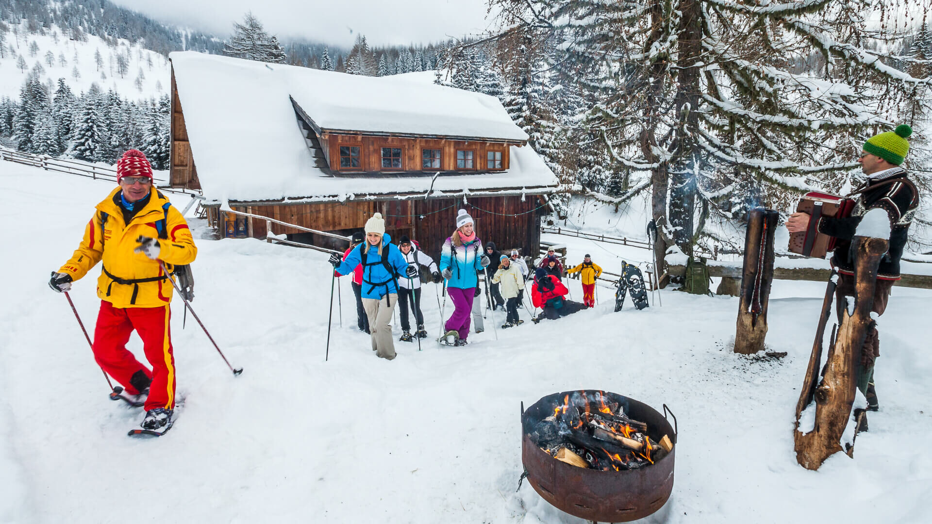 Escursionisti con le ciaspole presso una baita innevata con braciere